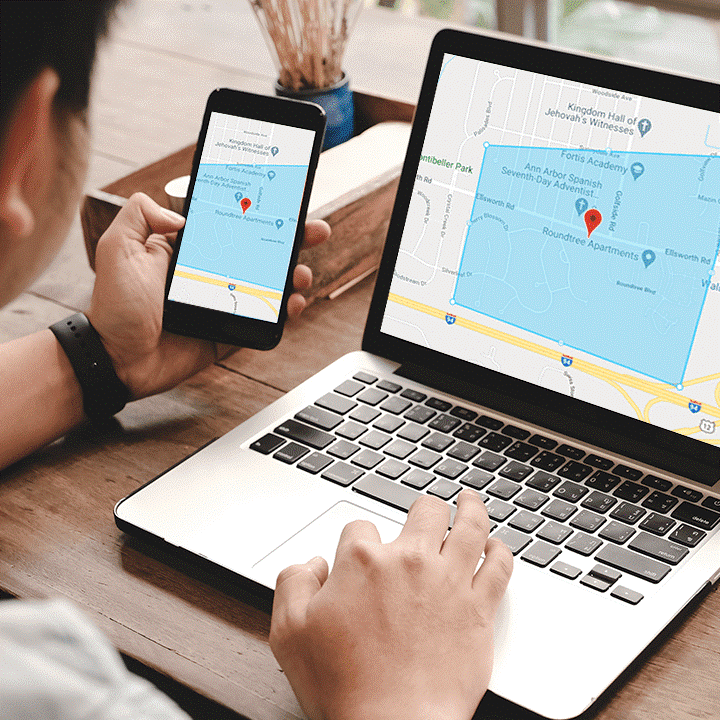 Man Typing on a Laptop with One Hand While Holding His Phone in the Other with Google Maps Pulled Up on Both Screens