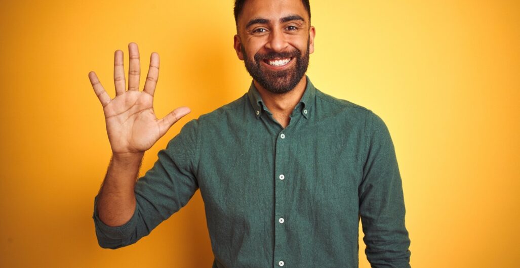 A smiling man wearing a green button-down shirt while holding up the five fingers of one hand.