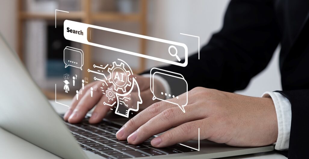 Hands typing on a keyboard of a laptop with a virtual search bar hovering above with a symbol for AI to indicate generative AI.