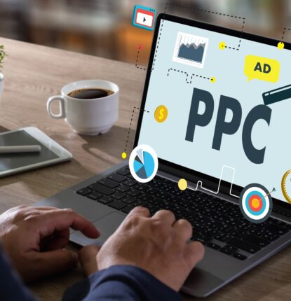 A man’s hands hover over a laptop keyword with digital graphics and the word ”PPC” floating off of the laptop screen